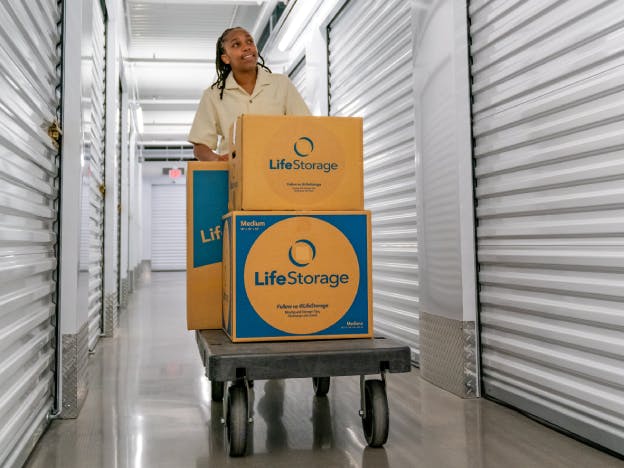 Man pushing a cart of Life Storage moving boxes in various sizes down a storage facility hallway.