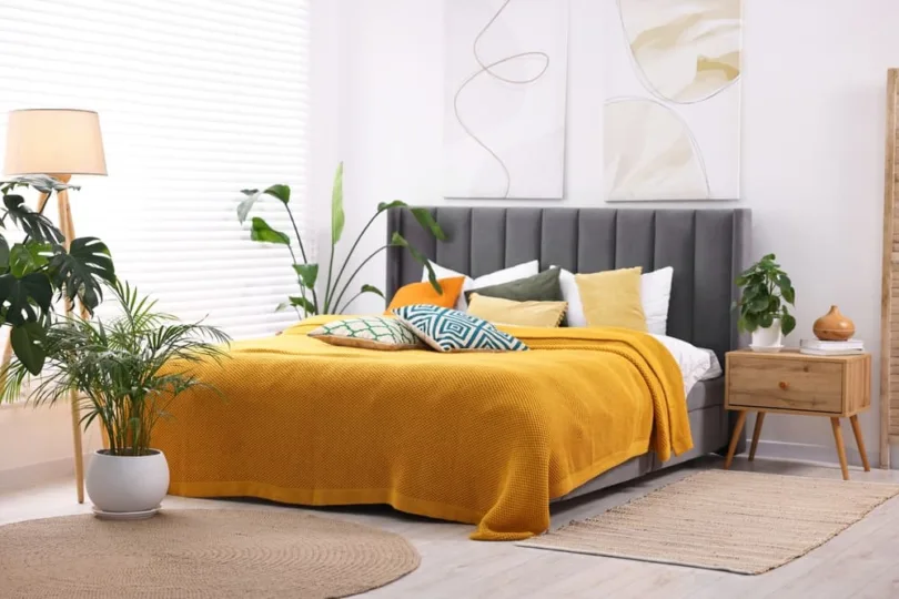 Bed with gray upholstered headboard and yellow comforter in the middle of staged bedroom